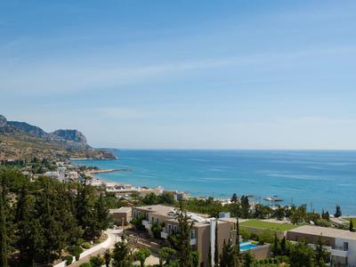 Pohled na moře s pobřežím, stromy a budovami pod modrou oblohou.