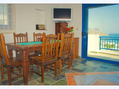 Jídelna s dřevěným stolem, židlemi, TV a balkonem s výhledem na moře.