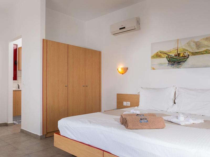 Jednoduchý hotelový pokoj s manželskou postelí, skříní, klimatizací a obrazem moře na stěně.