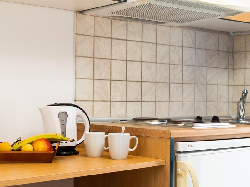 Malá hotelová kuchyň s miskou ovoce, rychlovarnou konvicí, hrnky a sporákem.