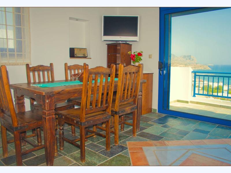 Jídelna s dřevěným stolem, židlemi, TV a balkonem s výhledem na moře.