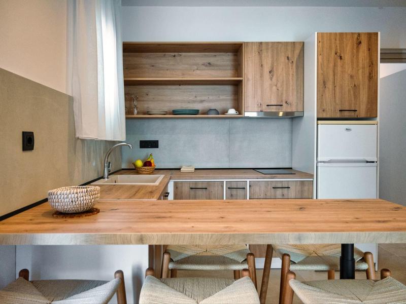 Moderní kuchyň s dřevěnou pracovní deskou a bílými spotřebiči v jasné místnosti s židlemi.