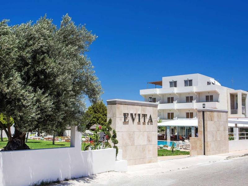 Complesso hotel moderno con cielo azzurro e grande albero all'ingresso.