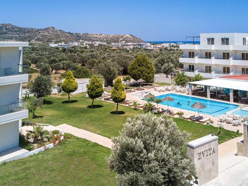 Vista di un hotel con piscina, giardino curato e montagne sullo sfondo con tempo sereno.