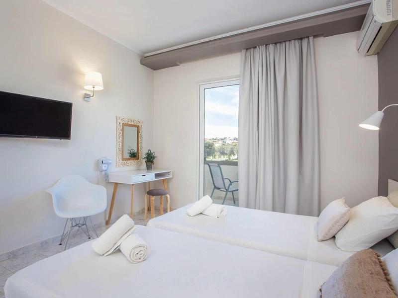 Camera d'hotel moderna con letto matrimoniale, TV, scrivania e balcone con tende.