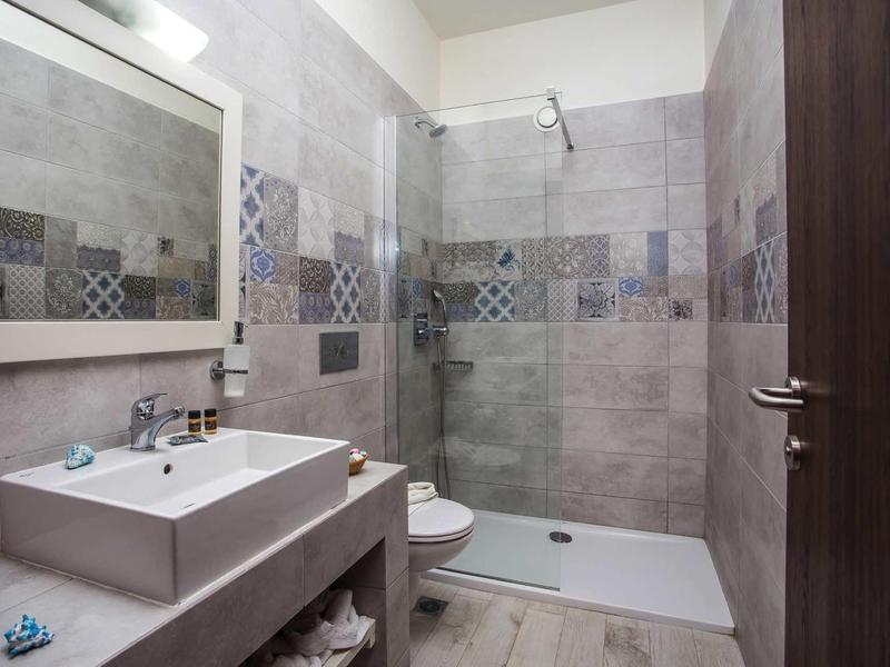 Bagno moderno con doccia, lavabo e WC, piastrelle grigie con accenti decorativi.