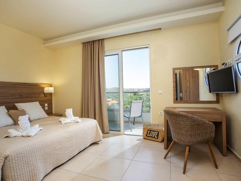 Camera d'hotel luminosa con due letti, scrivania, sedia, TV e balcone con vista.