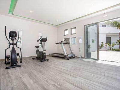 Palestra luminosa con attrezzature cardio e accesso a un cortile interno.
