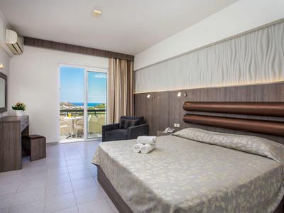 Camera d'hotel moderna con letto matrimoniale, zona salotto e balcone con vista mare.