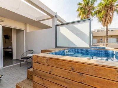 Vasca idromassaggio moderna su una terrazza con palme e porta aperta verso l'interno.