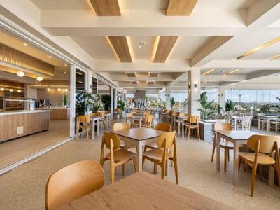 Helles, modernes Restaurant mit Holzstühlen, Tischen und großen Fenstern, viel natürlichem Licht.