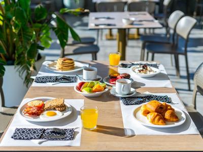 Un tavolo per la colazione apparecchiato con cornetti, frutta, succo e caffè all'aperto.