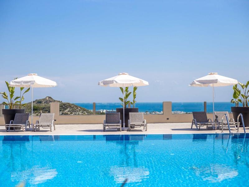 Piscina con lettini, ombrelloni e vista sul mare sotto un cielo limpido.