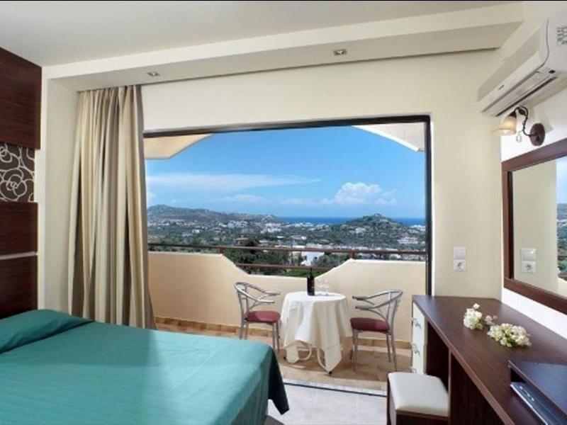 Camera d'hotel con balcone, tavolo e sedie, vista sulla città e sulle montagne con cielo sereno.