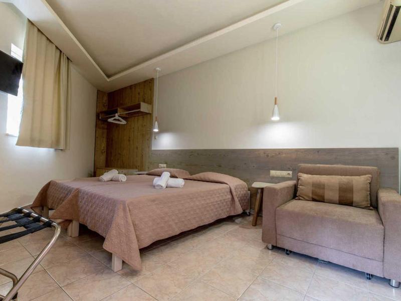 Una semplice camera d'hotel con letto matrimoniale, divano, lampade a muro e aria condizionata.