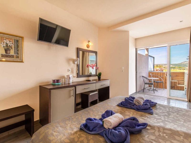 Camera d'hotel luminosa con letto matrimoniale, TV, scrivania e balcone con posti a sedere.