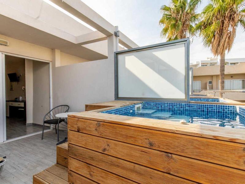 Vasca idromassaggio moderna su una terrazza con palme e porta aperta verso l'interno.