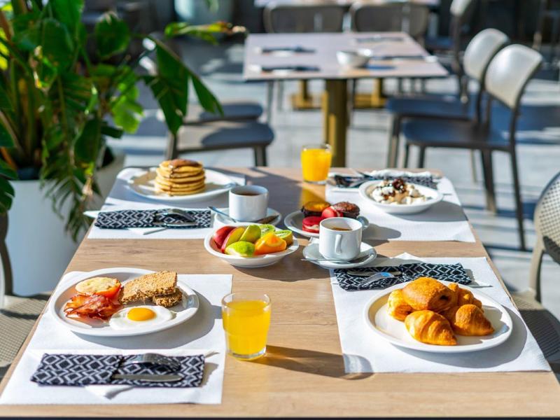 Un tavolo per la colazione apparecchiato con cornetti, frutta, succo e caffè all'aperto.