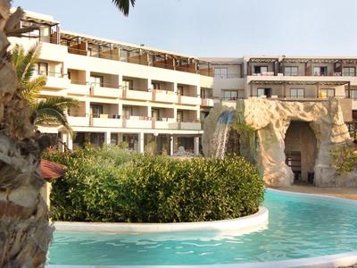 Ein Hotel mit mehreren Stockwerken, tropischer Pool und leichter Palmenblick im Sonnenschein.