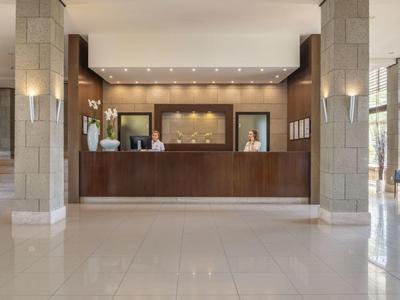 Grande réception d'hôtel avec comptoir en bois sombre et deux réceptionnistes, couloir lumineux