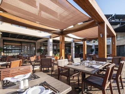 Restaurant en plein air avec mobilier en bois et toiles d'ombrage par jour ensoleillé.