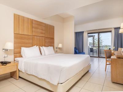 Jasny pokój hotelowy z dużym łóżkiem, drewnianymi akcentami i balkonem z widokiem na przyrodę.