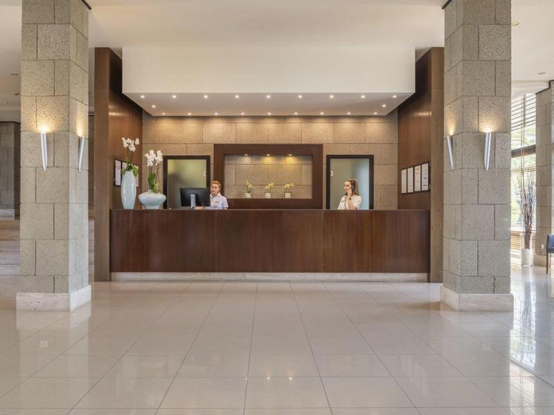 Przestronna recepcja hotelowa z ciemnym drewnianym kontuarem i przyjaznym personelem.