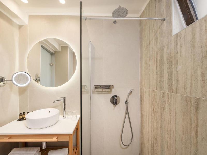 Jasna łazienka z umywalką, podświetlanym lustrem i prysznicem z przeszkloną ścianką.