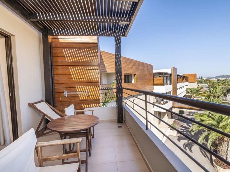 Balkon z dwoma drewnianymi krzesłami i stołem z widokiem na nowoczesną elewację i palmy.