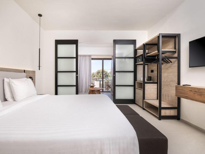 Nowoczesny pokój hotelowy z dużym białym łóżkiem, przechowywaniem w stylu loft i telewizorem.