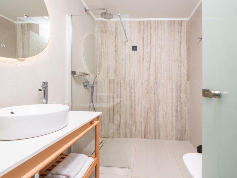 Jasna łazienka hotelowa z okrągłą umywalką i prysznicem typu walk-in z drewnianą ścianą dekoracyjną.