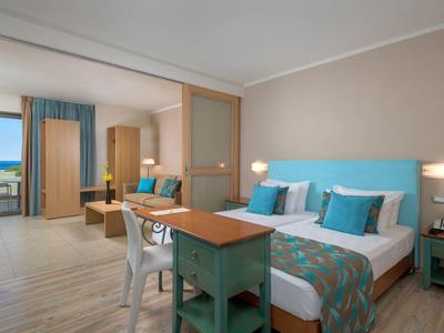 Hell eingerichtetes Zweibettzimmer mit Holzmöbeln, türkisfarbenen Akzenten und schönem Ausblick.