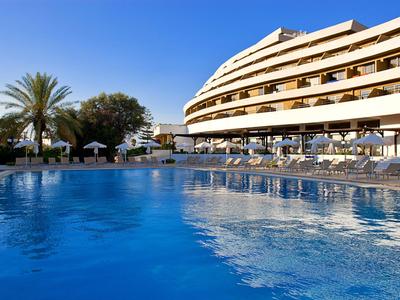 Groot buitenzwembad voor een modern hotel met parasols en palmbomen bij heldere lucht.
