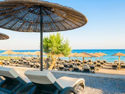 Lege ligstoelen onder stro parasols op een kiezelstrand met uitzicht op zee.