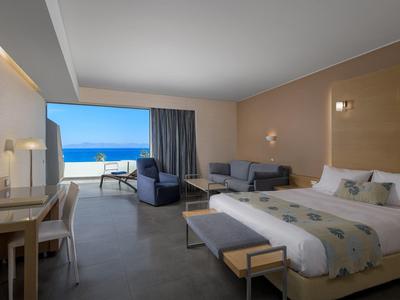 Modernes Hotelzimmer mit Doppelbett, Couch, Schreibtisch und Meerblick durch große Glaswand.