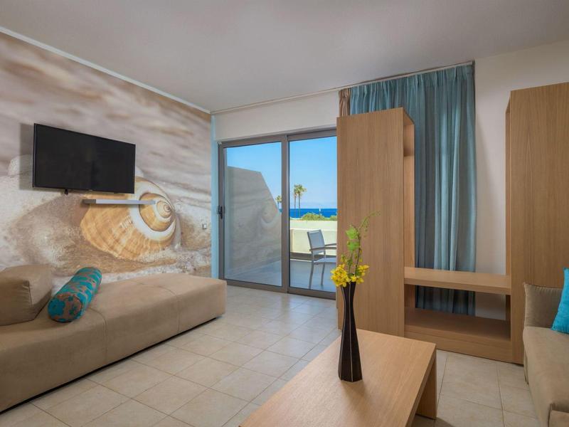 Helles Wohnzimmer mit zwei beigen Sofas, bunten Kissen, Holzvertäfelung und großem Balkonfenster.