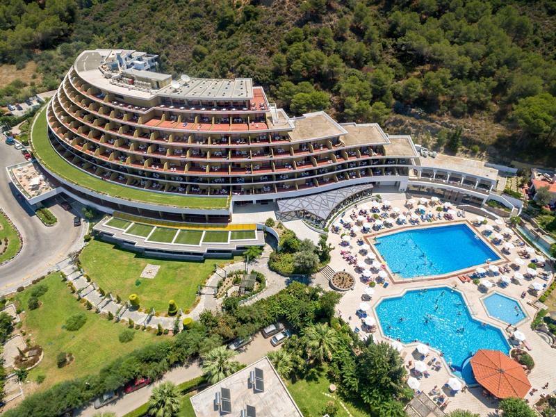 Großes, geschwungenes Hotel mit zwei blauen Pools, umgeben von grüner Vegetation.