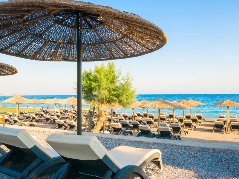 Strand mit Liegestühlen, Sonnenschirmen aus Stroh und blauem Meer unter klarem Himmel.