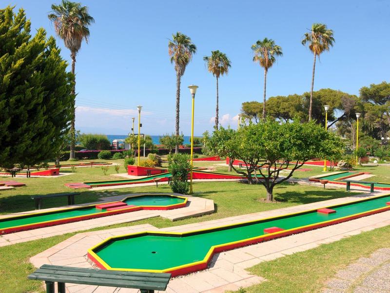 Mehrere Minigolfbahnen mit grünen Spielfeldern und roten Rändern im sonnigen Freien.