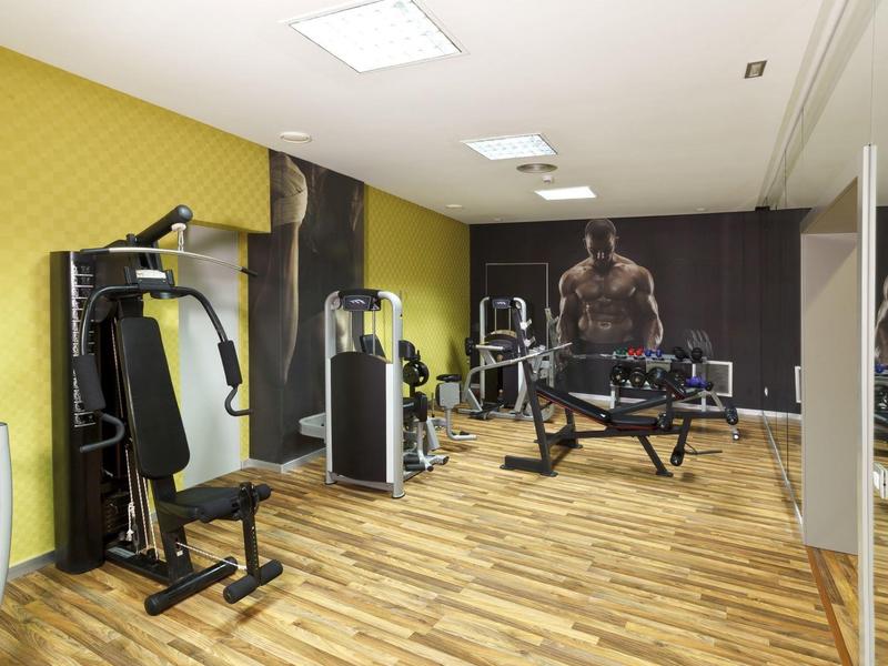 Moderner Fitnessraum mit Holzfußboden, gelber Wand und verschiedenen Trainingsgeräten.