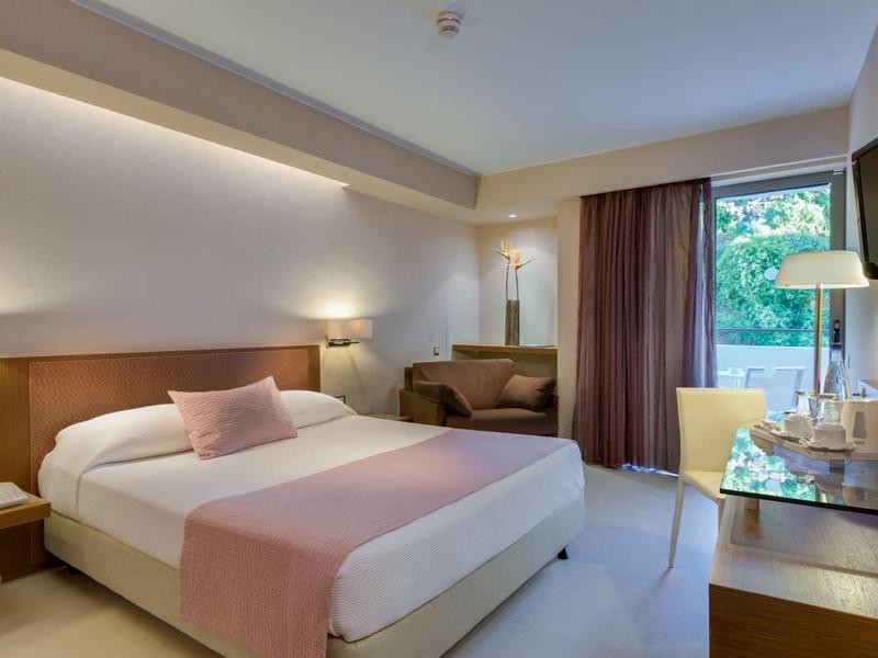 Modernes Hotelzimmer mit großem Bett, dunklen Vorhängen, Schreibtisch und TV an der Wand.