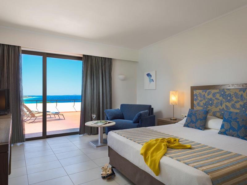 Modernes Hotelzimmer mit Doppelbett, Sofa, Zugang zur Terrasse und Meerblick bei Tageslicht.