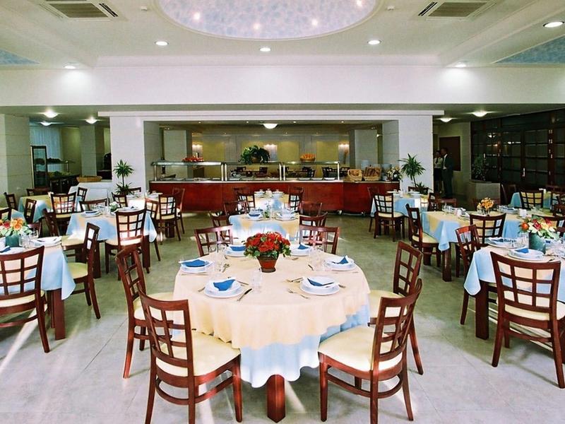 Grande salle à manger d'hôtel avec des tables rondes et des chaises en bois sur un sol en bois.