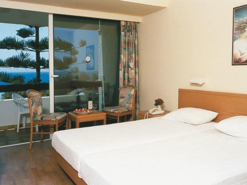 Chambre d'hôtel lumineuse avec lit double, coin salon et balcon avec vue sur la mer.