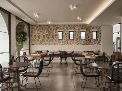 Modern café with wire chairs and tables in front of a patterned wall with small windows.
