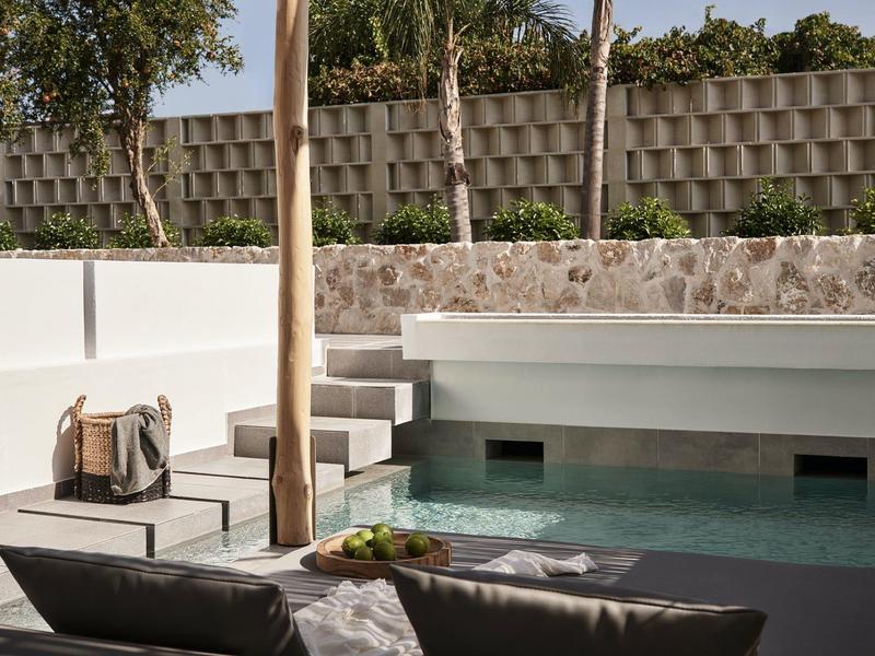 Piscina esterna moderna con pareti bianche, posti a sedere accoglienti e ambiente verde.