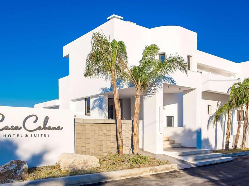 Moderno edificio alberghiero bianco con palme e cielo azzurro limpido.
