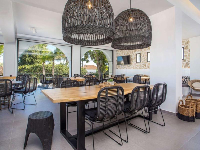 Sala da pranzo luminosa con sedie in legno e metallo, grandi finestre e lampade a sospensione in vimini.