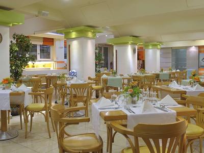 Restaurante luminoso con muchas mesas y sillas de madera, con manteles blancos y servilletas.