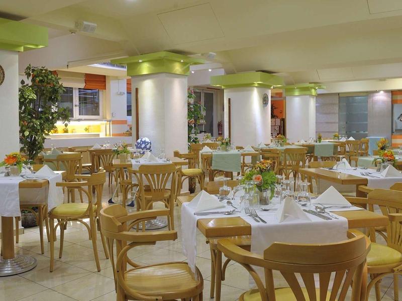 Licht, ruim restaurant met houten tafels en stoelen bedekt met witte doeken.